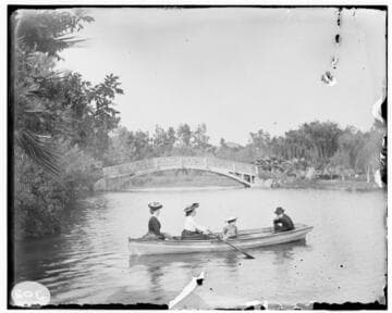 A family taking a small boating excursion in a calm pond with trees surrounding the water and a bridge in the background