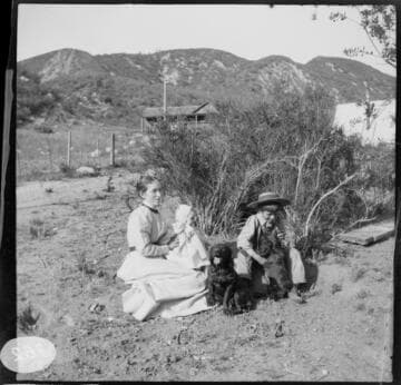 A woman sitting in the dirt with a baby on her lap and a young boy at her side