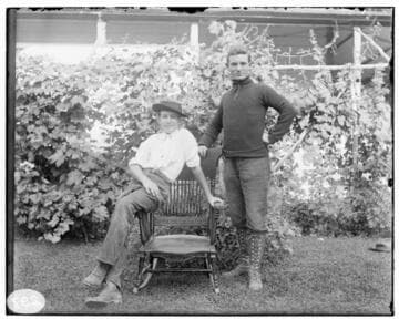Two men posed in front of a residence; the men are the same men as in the past two pictures