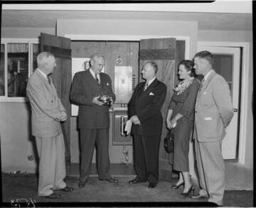 Three Edison men presenting  "one millionth" meter to owners in back yard of home