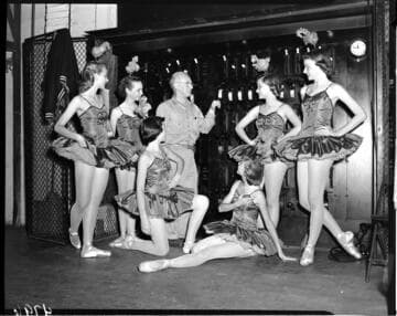 Man standing by switch panel surrounded by 6 young ballerinas in tutus