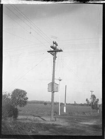 Double circuit wood pole distribution lines with junction pole and communications boxes (?) and light on nearest pole