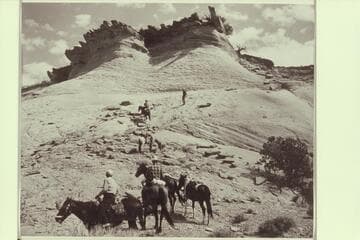 Buck White-hat rides up the slickrock to the mesa in front of Arch in the Sky