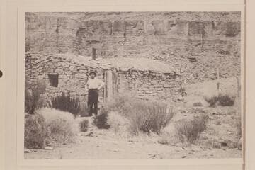 E. E. Spencer standing in front of Mendenhall cabin on the San Juan River.  E. E. Spencer had come down from Salt Lake to visit Arthur Spencer at his trading post at Mexican Hat
