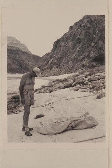 John Doerr examines the life raft lost by the Scout troop in Glen Canyon and found by the Nevills party at Mile 219 in 1948, July; Diamond Creek