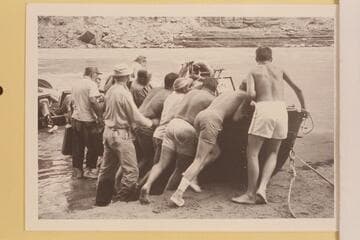 The Marston-Disney crew rolling a boat at Mile 166.  Doc Reed holds the jeep cans.  Jim Algar can find no room to get in.  Russ Haverick, Garth Marston and Les Gear are in there pitching.  Buzz Belknap lacks leverage