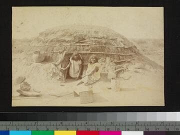 Two Southwest Indian women seated in front of a hogan or dwelling