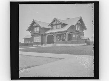 Unidentified two-story house with large lawn and new trees, street view