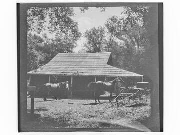 People with two horses near a carriage and stable(?)