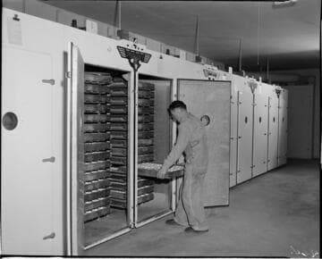 Farmer placing rack of eggs into cabinets (for cold storage or incubation?)