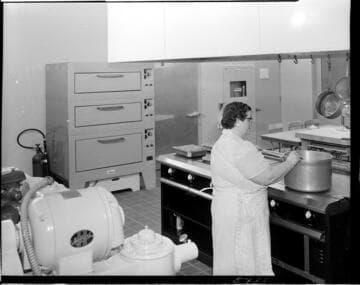 Chef cooking with a large pot on electric range in commercial grade kitchen
