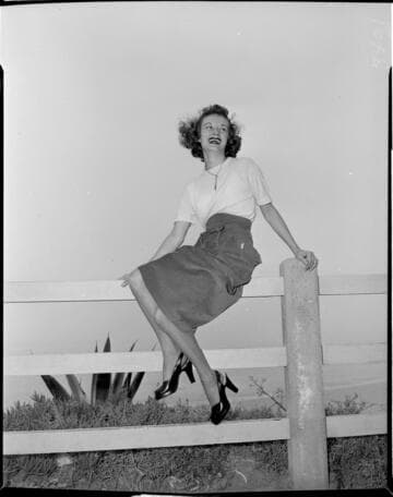 Young lady in a skirt posed sitting on a fence rail overlooking the beach