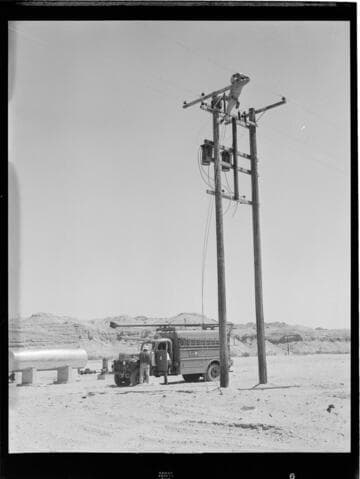 Linemen installing transformers on a pair of distribution poles in the desert