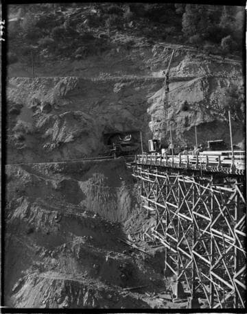 Big Creek 4 construction work: closer shot of bridge structure and mouth of power tunnel.  Tunnel mucker is dumping a load of tailings into dump truck at mouth of tunnel