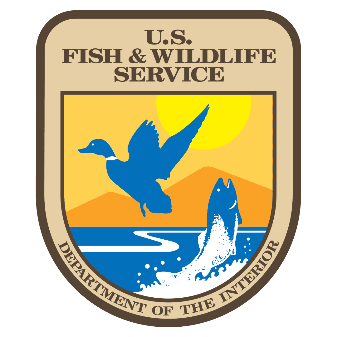 A shield-shaped logo with a brown background and text reading " U.S. Fish & Wildlife Service" with a blue and yellow vector illustration of a flying duck and jumping fish.
